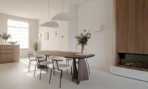 Eettafel met stoelen in een modern, licht interieur. Een vaas met bloemen en een kaars op tafel. Een gashaard met houten ombouw. Dit feng shui huis straalt rust uit.