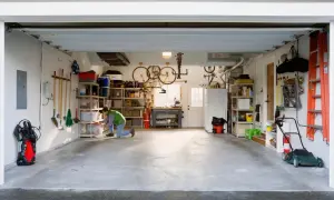 Een man richt een kleine garage in. Fietsen hangen aan het plafond, gereedschap hangt aan de muur en er staan opbergkasten vol spullen.
