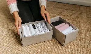 Handen sorteren opgerolde kleding in opbergdozen. Een slimme manier om je huis netjes te houden met deze huishouden tips.