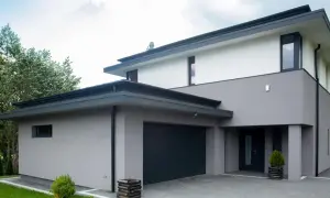 Moderne woning met grijze buiten stuc, donkere garagepoort en entree. Omringd door groen.