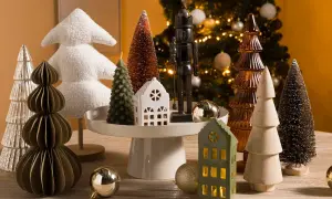 Kerstboom decoratie in Scandinavische stijl: diverse kerstboompjes, een notenkraker en huisjes op een houten tafel.