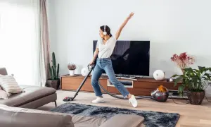 Vrolijke vrouw met koptelefoon danst tijdens de voorjaarsschoonmaak met de stofzuiger.