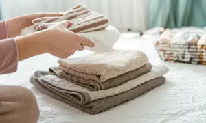 Handen vouwen gestreepte en effen handdoeken. De stapel handdoeken op het bed is zo netjes, dat ze bijna niet drogen.