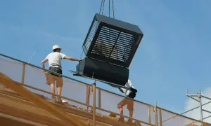 Bouwvakkers plaatsen een grote, prefab ventilatie-unit op een dak. Dit laat zien hoe wat is prefab: kant-en-klare onderdelen die snel gemonteerd worden.
