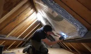 Man isoleert de zolder met reflecterend materiaal. Zo wordt de warmte in huis gehouden en bespaart hij op energiekosten.