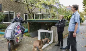 Een vader met dochter in bakfiets, zoon en hond staan buiten. Een slimme oplossing voor fietsen in de voortuin, met een groen dak boven de stalling.