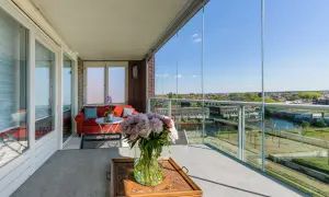 Een prachtig uitzicht vanaf dit balkon, dat met glazen schuifwanden is dichtgemaakt. Een rode bank en bloemen maken het gezellig.