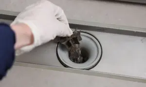 Hand met handschoen trekt haren uit een verstopt doucheputje.