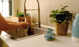 Iemand is bezig met het wasbak keuken schoonmaken. Water stroomt uit de kraan terwijl de handen een spons vasthouden.