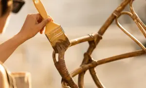 Hand met kwast werkt aan het **zelf rotan stoel repareren**. De stoel krijgt een opknapbeurt.