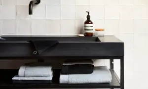 Stapel donkere handdoeken wassen en lichte handdoeken op een plank onder een zwarte wastafel.