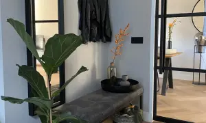 Een mooie hal met een grote plant, leren jasjes aan de kapstok, een bankje en een mand.