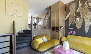 Gezellige split level woning met gele bank, trap en opvallende muurdecoratie.
