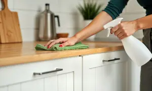 Een hand met rode nagellak spuit reinigingsmiddel op het aanrecht voor het bovenkant keukenkastjes schoonmaken.