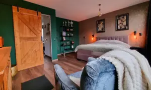 Slaapkamer met groene muur, houten schuifdeur en een bed met een deken met een subtiel ombre effect.