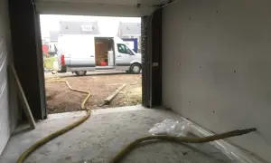 Grote gele slang voor zand stralen in een garage, met een busje buiten.