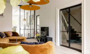 Gezellige woonkamer met oranje bank, glazen deuren naar de trap en een ontspullen lijst.