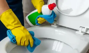 Gele handschoenen maken de wc vloer schoon met een blauwe doek en schoonmaakmiddel.