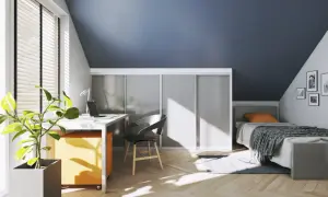 Een smalle hal met een bureau, bed en kasten. De zon schijnt door het raam en werpt patronen op de houten vloer.