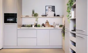 Moderne nis keuken met ingebouwde oven, strakke kasten en decoratieve planten. Een poster met een lachende vrouw siert de muur.