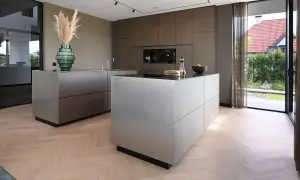 Moderne keuken met strakke, metalen kasten op een visgraat houten vloer. Een groene vaas met pampasgras siert het aanrecht.