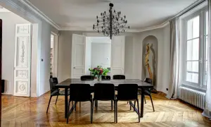 Elegant Frans interieur met een grote eettafel, zwarte stoelen, een opvallende kroonluchter en een houten vloer.