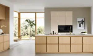 Een lichte, minimalistische keuken met houten kasten, een groot raam en een groene plant.