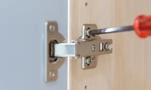 Met een schroevendraaier worden twee schroeven van een scharnier bijgesteld om de kastdeur perfect te laten sluiten.