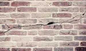 Een oude bakstenen muur met duidelijke scheuren die door de stenen lopen, getuigen van de tand des tijds.