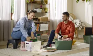 Een stel pakt spullen in, klaar voor hun reis van ontspullen in 52 weken. Ze sorteren boeken en kleding in opbergbakken.