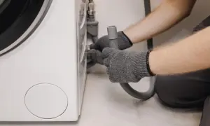 Grijze handschoenen bevestigen een slang aan een wasmachine, mogelijk om wasmachine problemen op te lossen.
