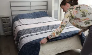 Vrouw verschoont bed met een bloemenblouse. Een schone slaapomgeving is belangrijk, dus vraag je je af hoe vaak bed verschonen?