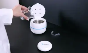 Een hand met een glas water vult een apparaat voor ultrasoon reinigen. Een bitje ligt ernaast.