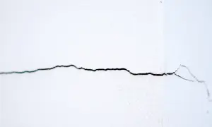 Een dunne, donkere horizontale scheur in een witte binnenmuur, die zich uitstrekt over het beeld.