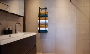 Netjes opgestapelde handdoeken in verschillende kleuren op een zwarte handdoekenrek in een moderne badkamer.