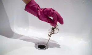 Roze handschoen verwijdert haar uit doucheputje om verstoppingen te voorkomen.