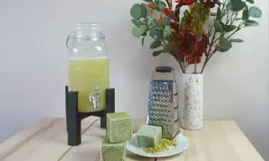 Zelf wasmiddel maken ervaringen: groene zeepblokken, rasp, en een glazen dispenser met gele vloeistof. Een vaas met herfstbladeren completeert het tafereel.