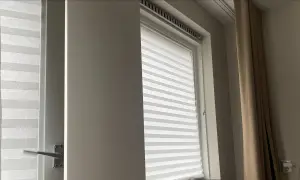 Wit plisségordijn als tijdelijke raambekleding tijdens een verbouwing. Een beige gordijn hangt ernaast.