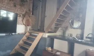 Een vide met een houten trap, bakstenen muur en een tv. Wat is een vide? Een open ruimte in een huis die meerdere verdiepingen verbindt.
