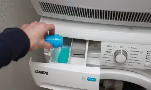 Hand giet blauw wasmiddel in het bakje van de wasmachine. Links of rechts, het bakje is duidelijk gemarkeerd.