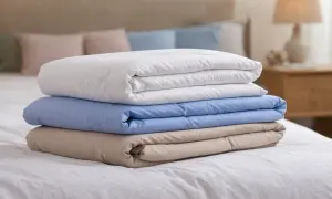 Stapel van drie opgevouwen dekbedovertrekken: wit, lichtblauw en beige. Ideaal om te weten hoeveel dekbedovertrekken je nodig hebt voor een frisse look.