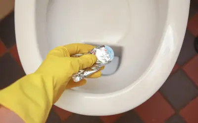 Gele handschoen houdt product vast om kalkrand wc pot te verwijderen.