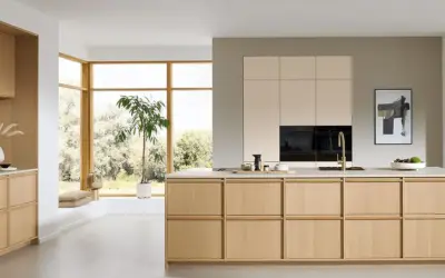 Een lichte, minimalistische keuken met houten kasten, een groot raam en een groene plant.