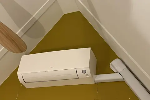Een witte airco unit met een Daikin logo, netjes gemonteerd. De airco leidingen zijn weggewerkt in witte kokers, wat zorgt voor een strakke afwerking.