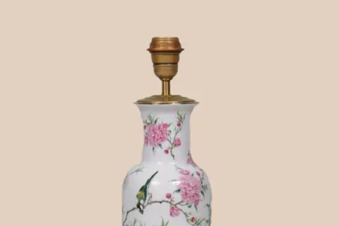 Een lamp maken van vaas: een witte vaas met roze bloemen en een vogel, omgebouwd tot lamp met een gouden fitting.