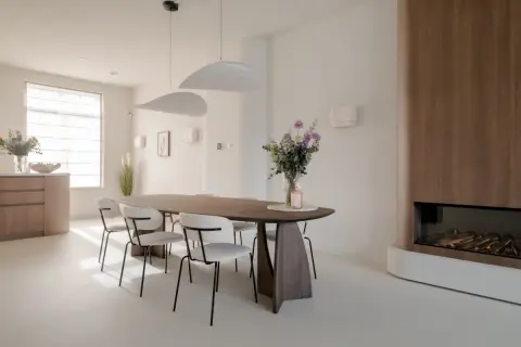 Eettafel met stoelen in een modern, licht interieur. Een vaas met bloemen en een kaars op tafel. Een gashaard met houten ombouw. Dit feng shui huis straalt rust uit.
