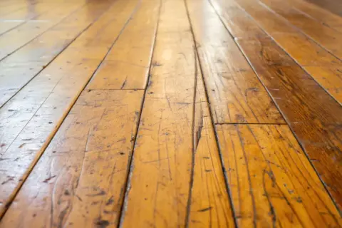 Gouden houten vloer met zichtbare krassen in gelakt hout, die verhalen vertellen van geleefde momenten.