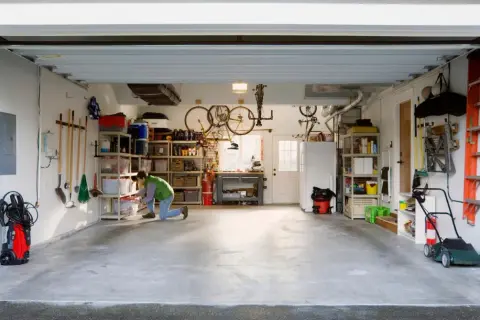 Een man richt een kleine garage in. Fietsen hangen aan het plafond, gereedschap hangt aan de muur en er staan opbergkasten vol spullen.