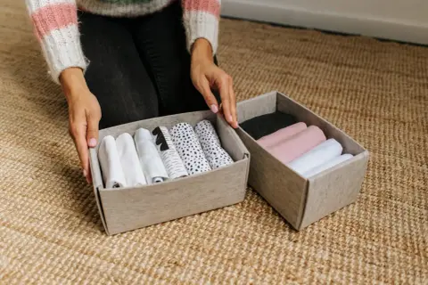 Handen sorteren opgerolde kleding in opbergdozen. Een slimme manier om je huis netjes te houden met deze huishouden tips.