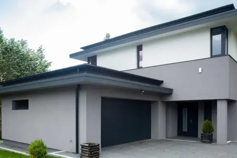 Moderne woning met grijze buiten stuc, donkere garagepoort en entree. Omringd door groen.